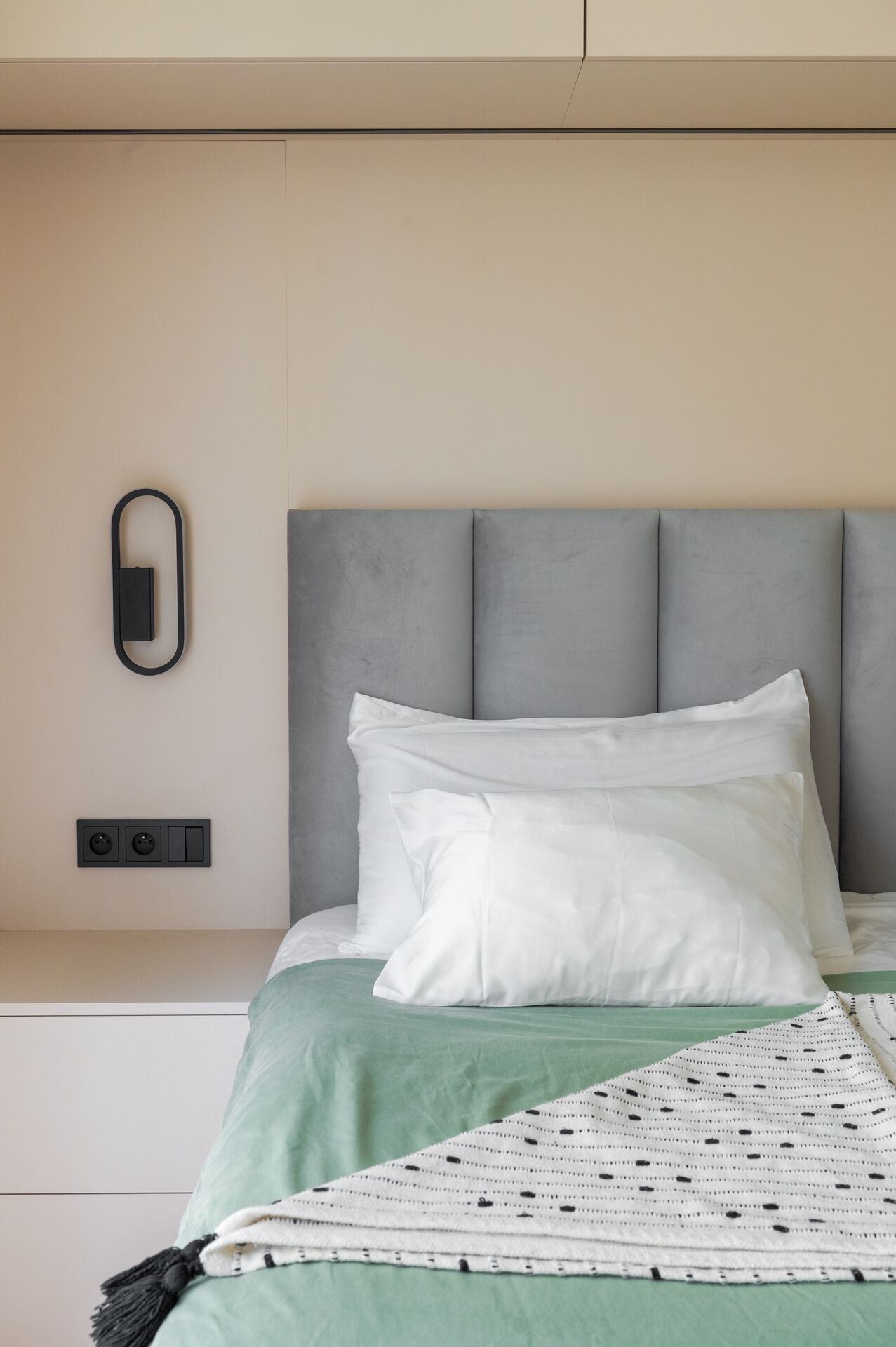 Detail of pillows and mint bedding on a bed with a grey upholstered headboard