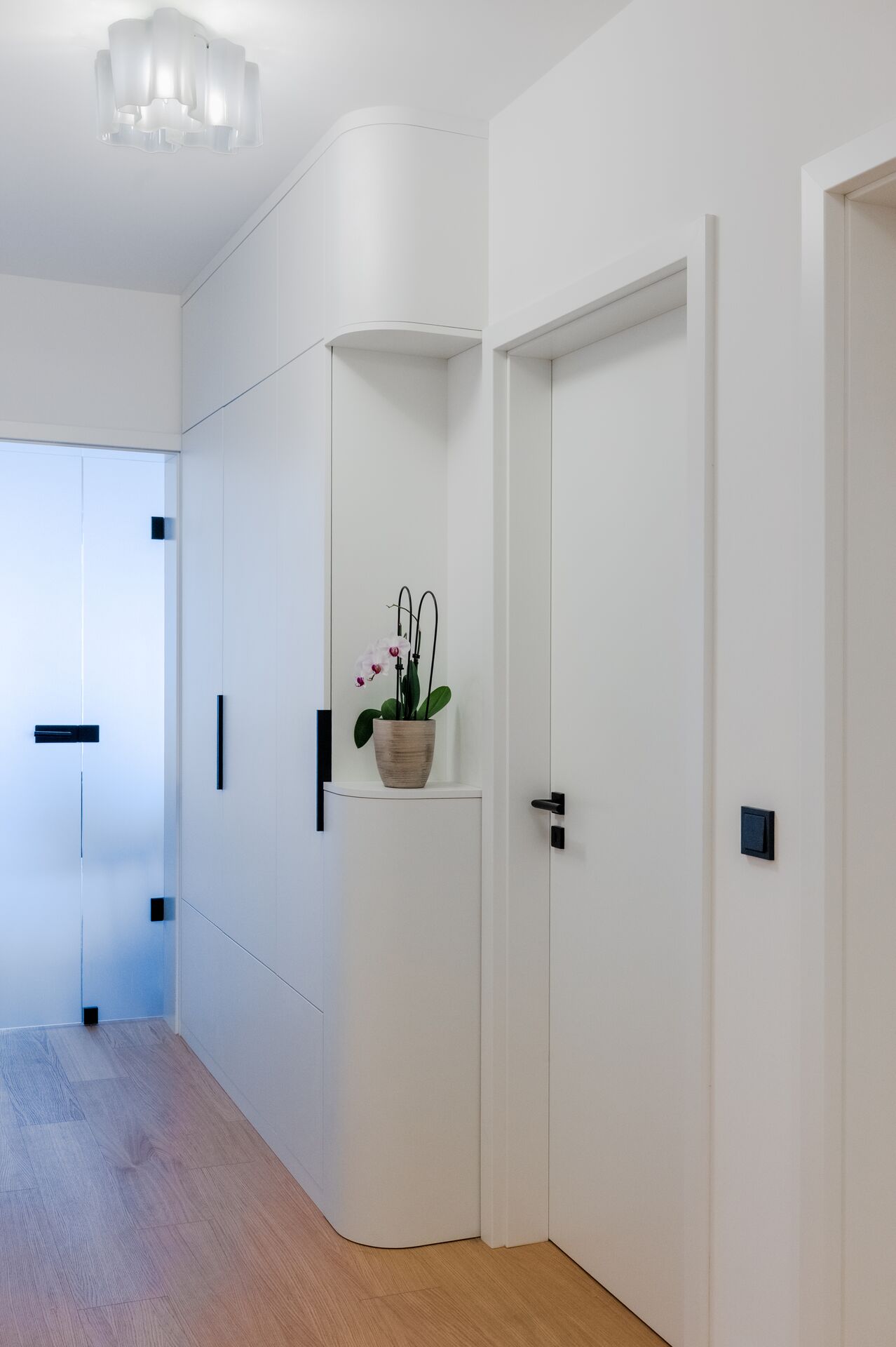 Hallway with oak flooring, white doors and an orchid on a cabinet