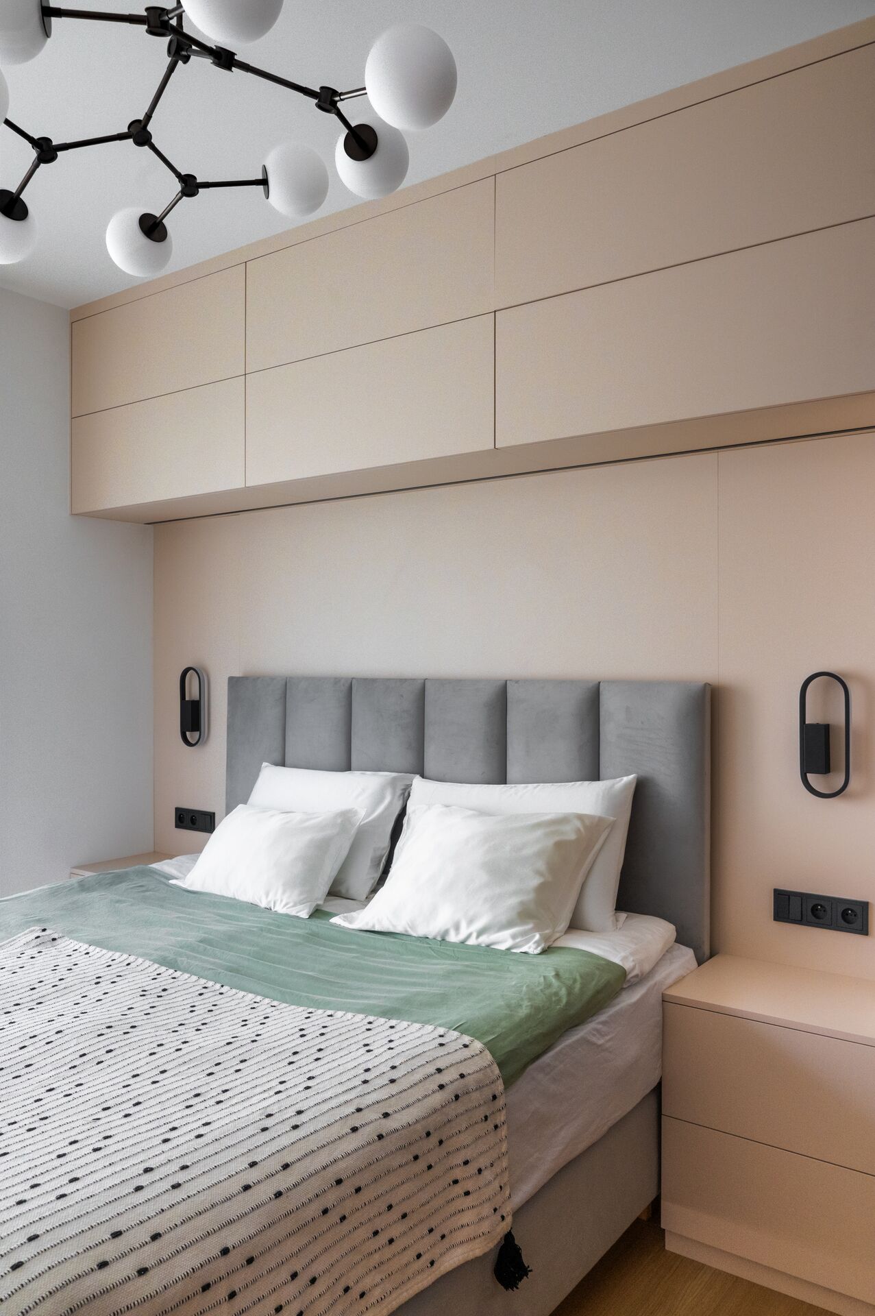 Bedroom with a grey upholstered headboard, mint bedspread and built-in cabinets above the bed
